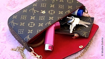 Eine Louis Vuitton Handtasche mit roten Innenleben. In der Tasche sind Schlüssel, ein Inhalator und eine Creme. 